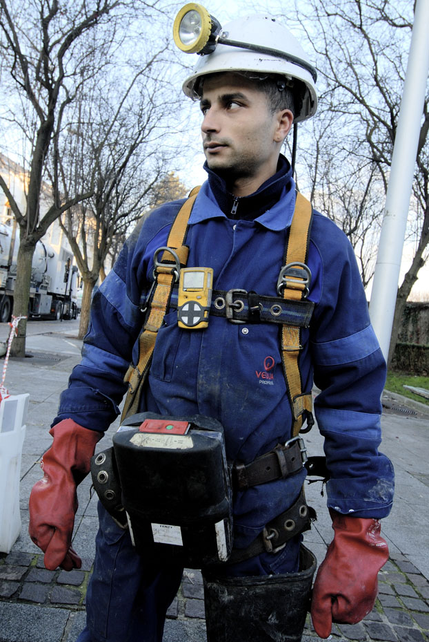 Opérateur se préparant à intervenir dans un réseau d’assainissement. Outre les équipements classiques, le travailleur porte un contrôleur d'atmosphère multigaz, un masque auto-sauveteur, et un baudrier antichute